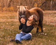 a woman kneeling down next to a brown horse