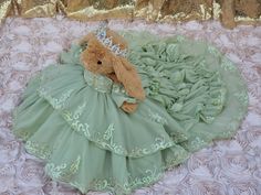 a teddy bear in a green dress laying on a bed with gold sequins