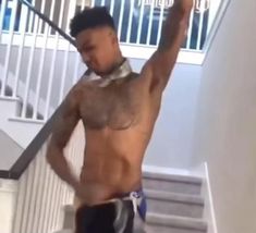 a man with no shirt on standing in front of stairs and holding his hand up