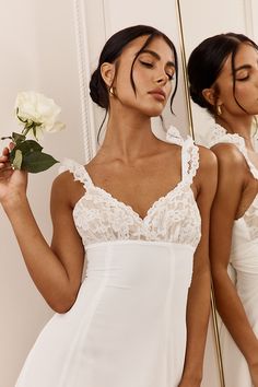 two women in white dresses holding flowers and looking at their reflection in the mirror with one woman's eyes closed