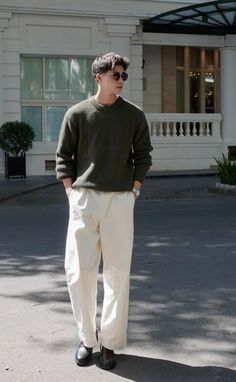 a man standing in front of a building wearing white pants and a green sweater with black shoes