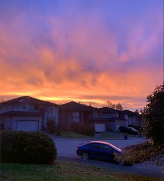 a blue car parked on the side of a road in front of houses at sunset