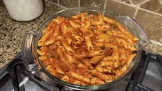 a glass bowl filled with pasta on top of a stove