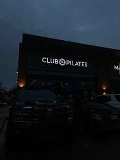 two cars are parked in front of a club pilates restaurant at night time