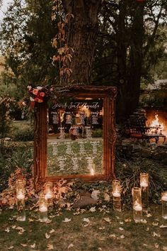 an outdoor ceremony with candles and a mirror on the ground in front of it, surrounded by trees