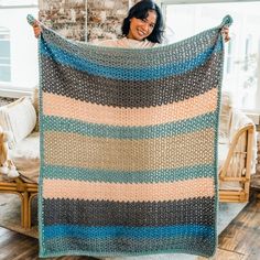 a woman is holding up a crocheted blanket