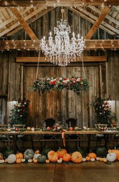 a table with chandelier and pumpkins on it in front of a wooden wall