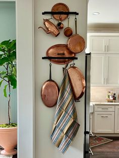 pots and pans are hanging on the wall next to a pot rack with copper cooking utensils