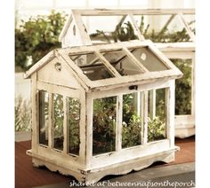 a small white house shaped planter with plants in it's roof and windows