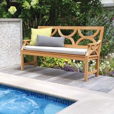 a wooden bench sitting next to a swimming pool with pillows on it's back