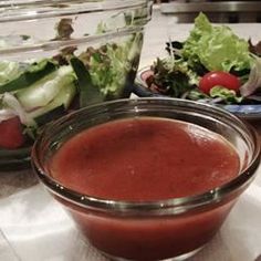 there is a bowl of tomato soup on the table next to some salads and lettuce