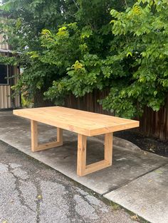 a wooden table sitting on top of a cement slab next to a fence and trees