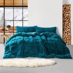 a bed covered in teal colored comforter next to a pile of firewood