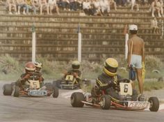 three people in go kart racing cars on a race track with spectators watching from the bleachers