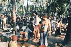 a group of people standing around each other in the sand near trees and palm trees