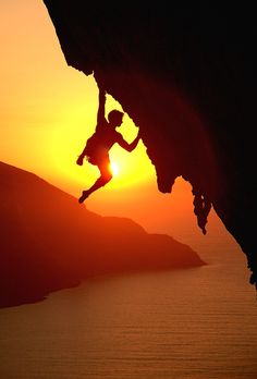 a man climbing up the side of a cliff at sunset