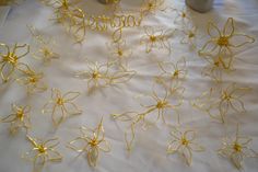 some gold wire flowers sitting on top of a white table cloth next to a cup