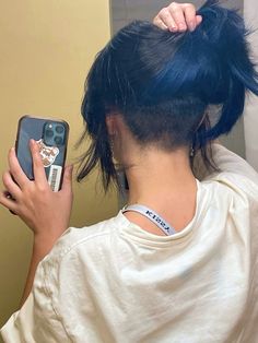 a woman with blue hair is looking at her cell phone and holding it in one hand