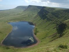 a large body of water sitting on the side of a lush green hill covered in grass