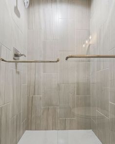 a walk in shower sitting next to a white tiled wall and floor with two handrails