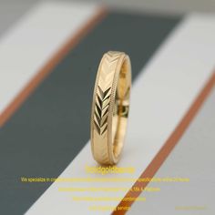 a gold wedding ring with an arrow design on it, sitting on a striped surface