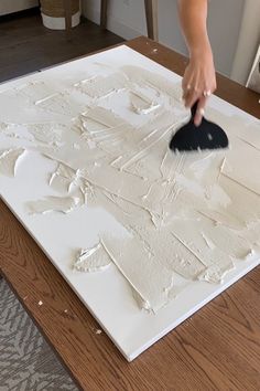 a person is using a brush to paint on a piece of white paper that has been placed on a table