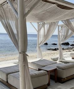 a bed sitting on top of a wooden floor next to the ocean with white curtains