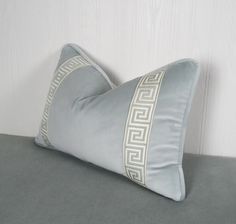 a light blue pillow with white greek border on the front and back of it, sitting on a gray surface