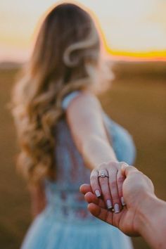 a woman holding the hand of a man's hand in front of an open field