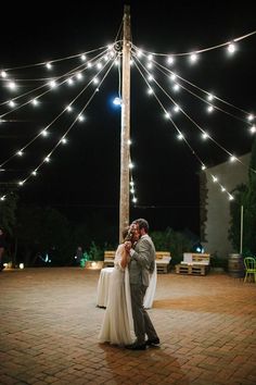 a bride and groom sharing a first dance under string lights