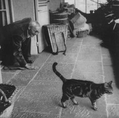 an old black and white photo of a man with a cat in front of him