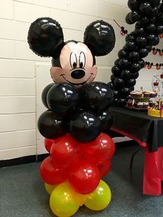 a mickey mouse balloon sitting on top of a table with black and red balloons around it