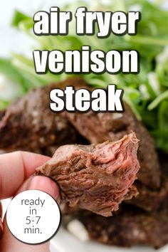 a hand holding a piece of steak over a white plate with greens on it and the words air fryer venison steak