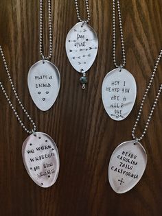 four different necklaces with words on them sitting on a wooden table next to each other