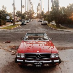 a red car parked on the side of a road next to trees and palm trees