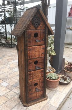 a wooden birdhouse sitting on the ground next to potted plants