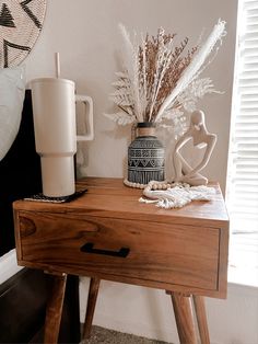 a wooden table topped with a vase filled with dried flowers and a coffee cup on top of it