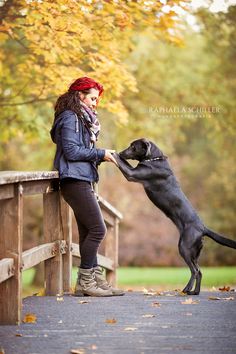 a woman and her dog playing with each other on a bridge in the fall leaves