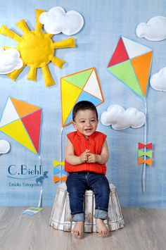 a little boy sitting on top of a chair in front of kites and clouds