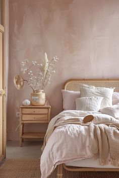 a bedroom with pink walls and white linens on the bed, along with a wicker headboard