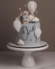 a blue cake decorated with hot air balloons and a teddy bear sitting on the top