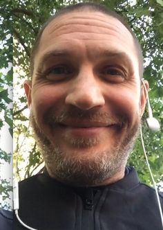 a close up of a person with ear buds in his ears and a tree behind him