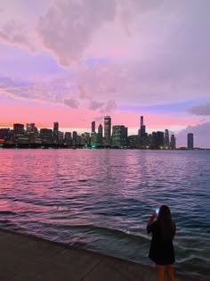 a woman standing on the edge of a body of water looking at the city skyline