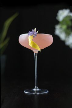 a pink cocktail with lavender garnish in a martini glass on a black table