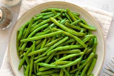 a white bowl filled with green beans on top of a table next to silverware