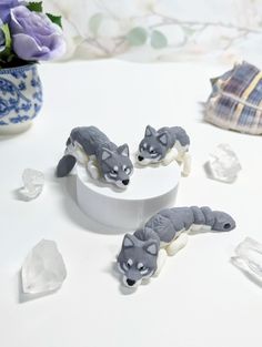 three small gray and white figurines sitting on top of a table next to flowers