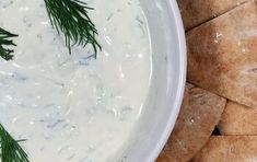 a white bowl filled with dip surrounded by crackers and dill sprigs