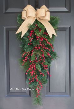 a christmas wreath with red berries and a bow hanging on the front door for decoration