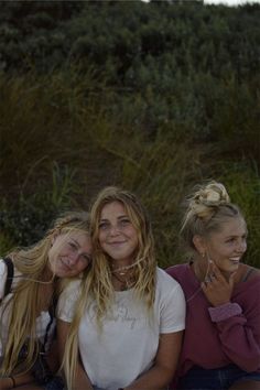 three young women sitting next to each other on the ground with grass in the background