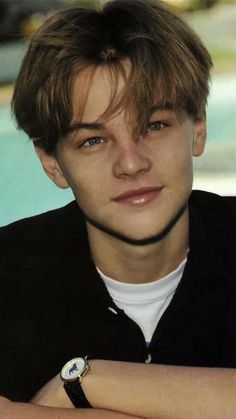 a young man with his arms crossed posing for a photo in front of a swimming pool